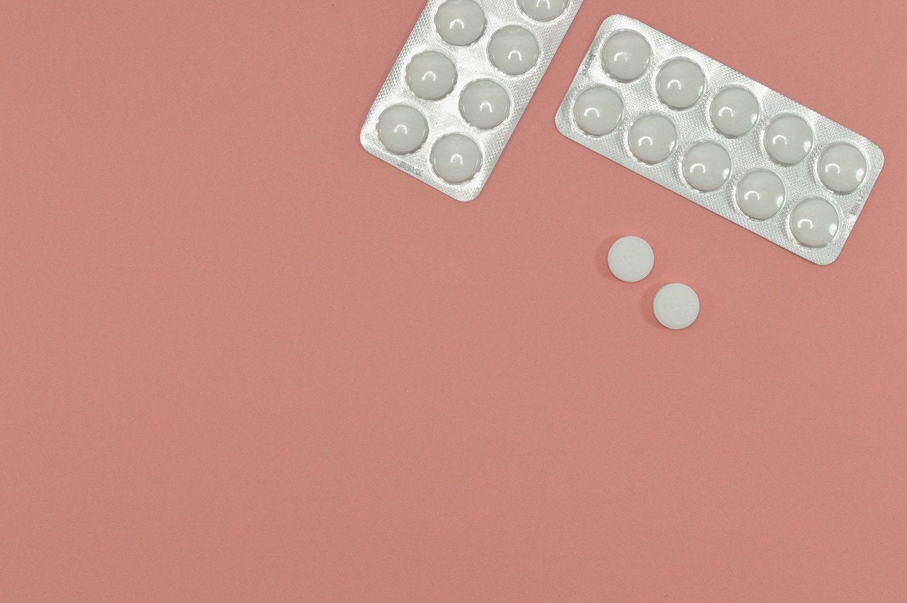 Two blister packs of pills and two loose pills on a pink background, illustrating the tapering of a medication dosage.