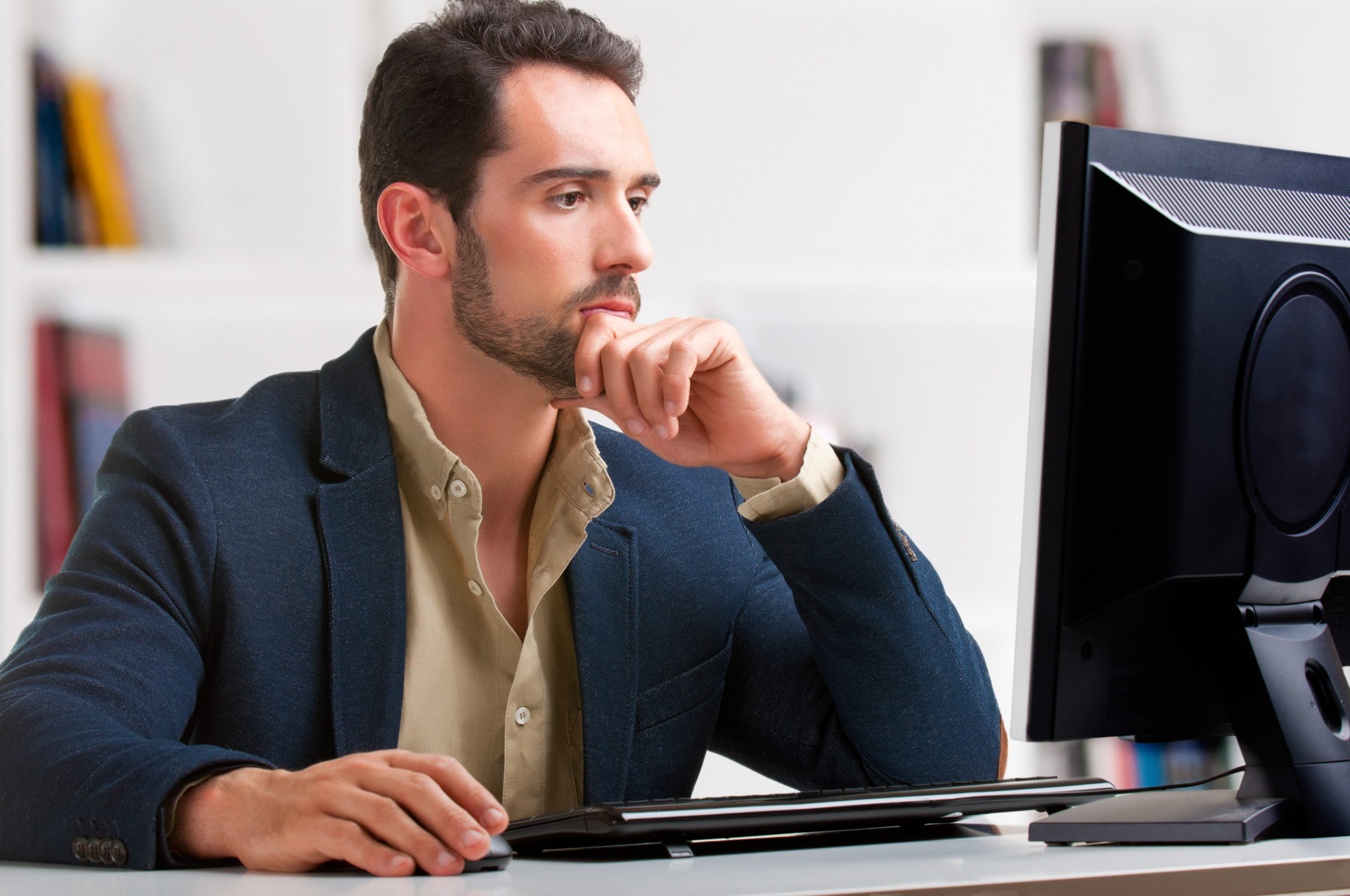 A man in a suit looking at a stock chart on a computer screen while holding his chin in thought.